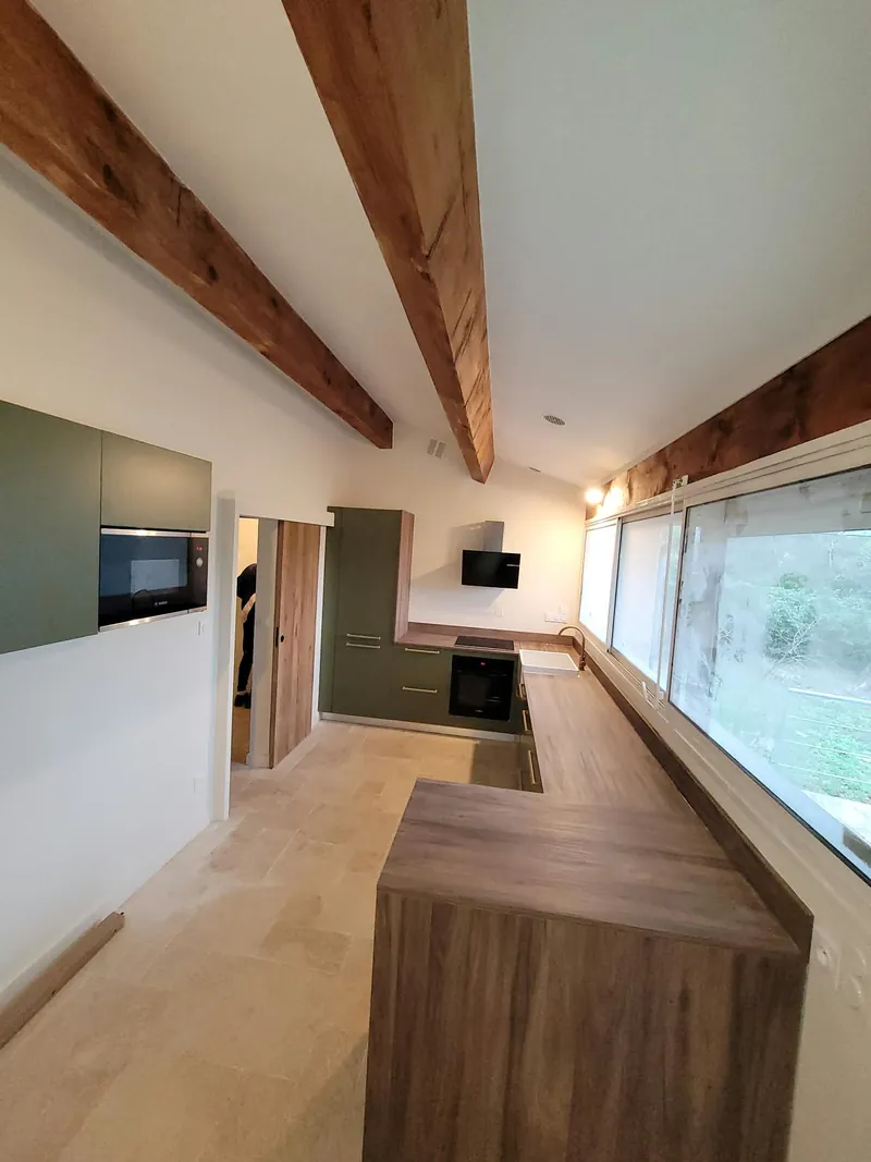 Cuisine équipée sous charpente apparente : meubles vert olive, plan de travail en bois et four encastré