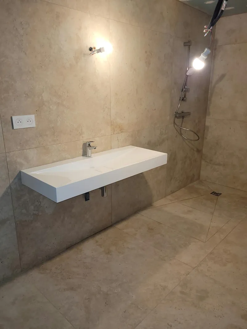 La même salle de bain terminée : carrelage effet pierre, plan vasque suspendu et douche à l’italienne