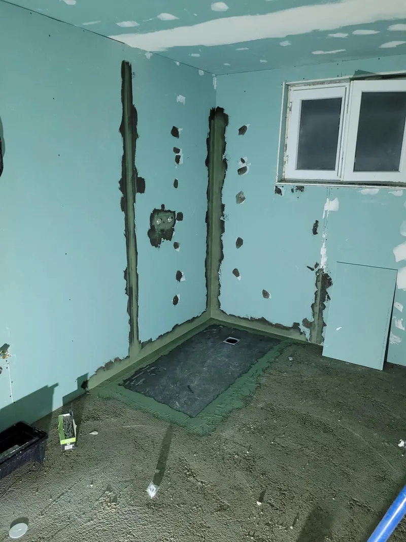 Salle de bain en travaux : murs étanchéifiés, sol brut et bonde de douche en attente